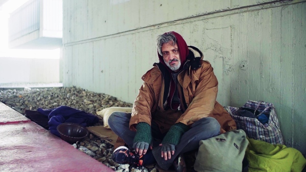 A portrait of tired homeless dirty beggar man sitting outdoors. Slow motion.