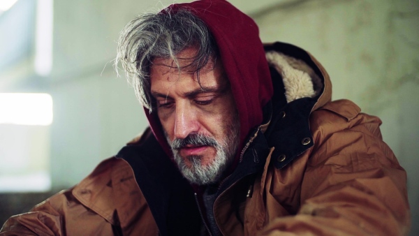 A close up portrait of homeless dirty beggar man sitting outdoors. Slow motion.