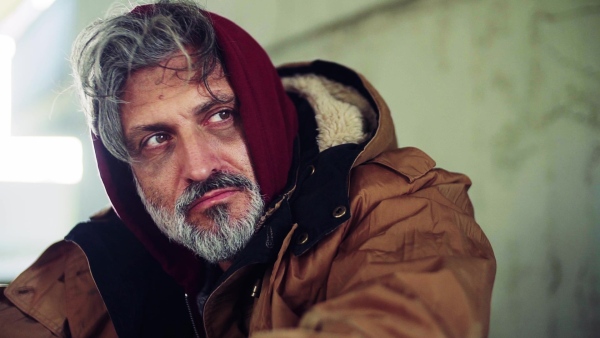 A close up portrait of homeless dirty beggar man sitting outdoors. Slow motion.