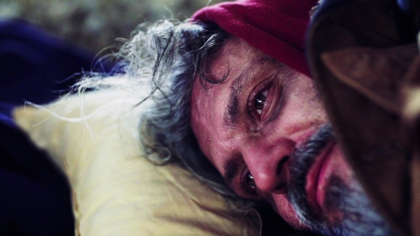 An extreme close up portrait of homeless dirty beggar man lying outdoors. Slow motion.