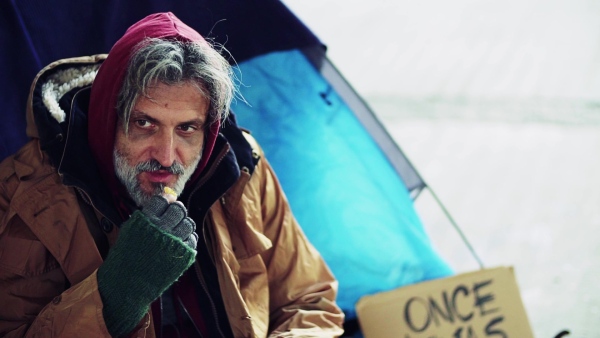 A frustrated homeless beggar man sitting outdoors, eating tangerine. Slow motion.