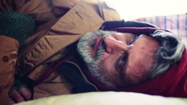 A close-up portrait of homeless dirty beggar man lying outdoors. Slow motion.