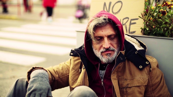 A close up portrait of homeless dirty beggar man sitting outdoors. Slow motion.