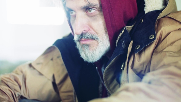 A close up portrait of homeless dirty beggar man sitting outdoors.