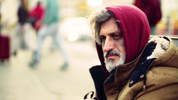 A close up portrait of homeless dirty beggar man sitting outdoors on the street. Slow motion.