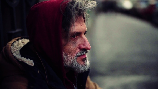 A close up portrait of homeless dirty beggar man sitting outdoors. Slow motion.