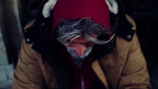 A close up portrait of homeless dirty beggar man sitting outdoors. Slow motion.