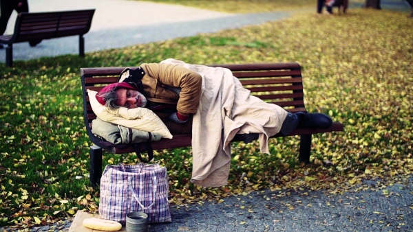 A homeless beggar man with a pillow lying on bench outdoors in city, sleeping. Slow motion.