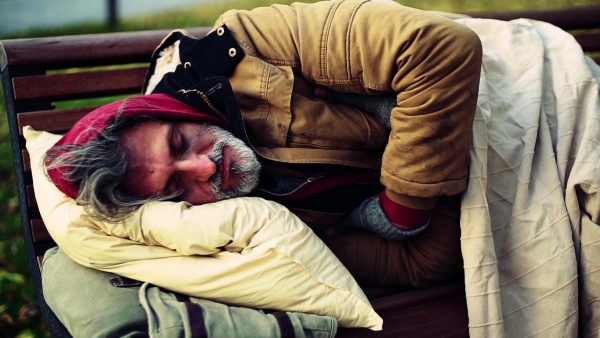 A homeless beggar man with a pillow lying on bench outdoors in city, sleeping. Slow motion.