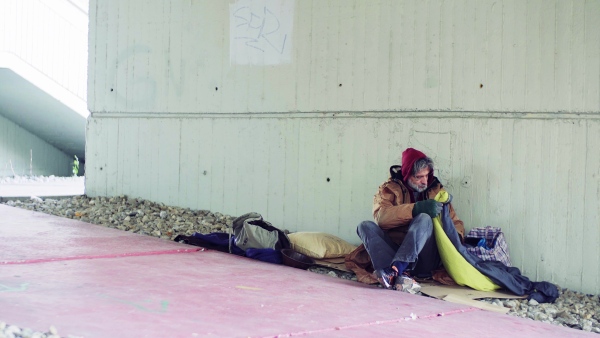 A portrait of homeless dirty beggar man lying down outdoors.