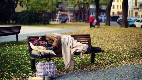 A homeless beggar man with a pillow lying on bench outdoors in city, sleeping. Slow motion.