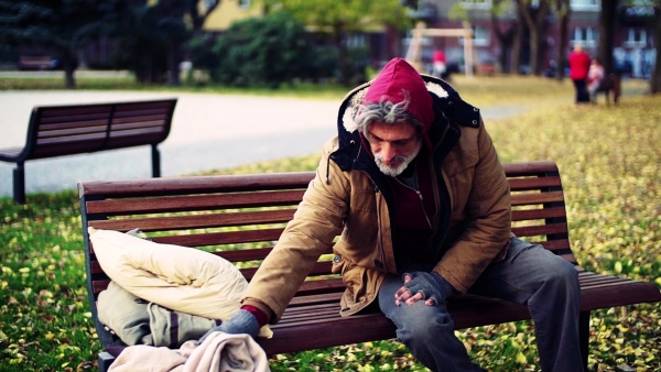 A homeless beggar man with a pillow lying on bench outdoors in city. Slow motion.