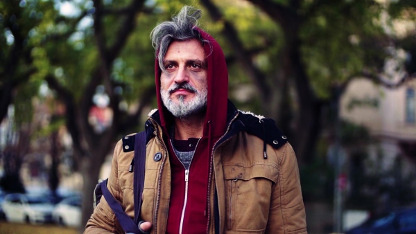 A portrait of homeless beggar man walking outdoors in park in autumn. Slow motion.