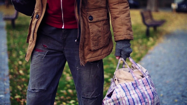 A midsection of portrait of homeless beggar man walking outdoors in park, carrying a bag. Slow motion.