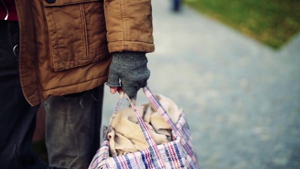 A midsection of portrait of homeless beggar man walking outdoors in park, carrying a bag. Slow motion.