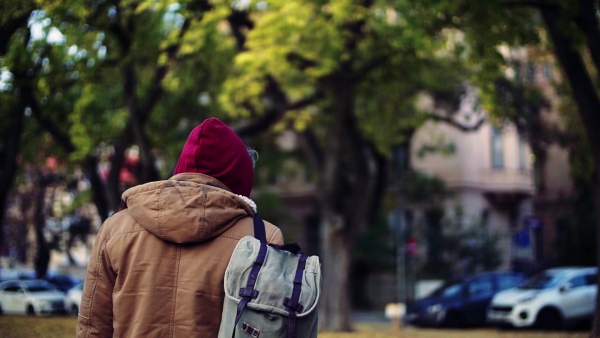 A rear view of homeless beggar man with hood on head walking outdoors in city, looking back. Slow motion.