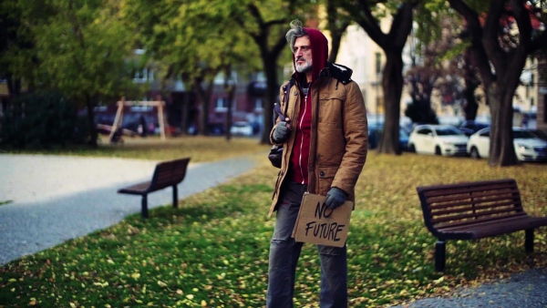 A portrait of homeless beggar man walking outdoors in park in autumn. Slow motion.