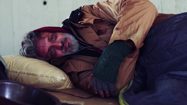 A portrait of homeless dirty beggar man lying outdoors.