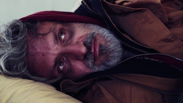 An extreme close-up portrait of homeless dirty beggar man lying outdoors.