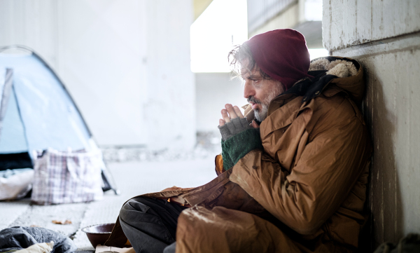 A homeless beggar man sitting outdoors in city asking for money donation.