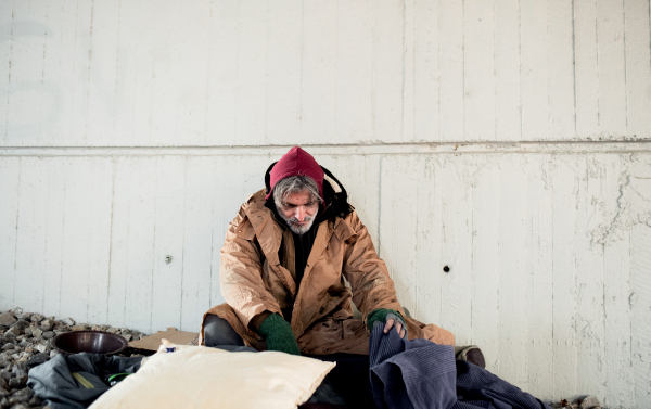 A homeless beggar man sitting outdoors in city asking for money donation.