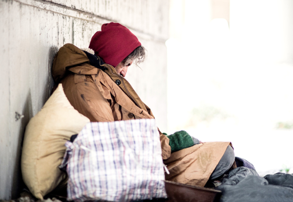 A side view of serious homeless beggar man sitting outdoors, leaning against a wall. Copy space.