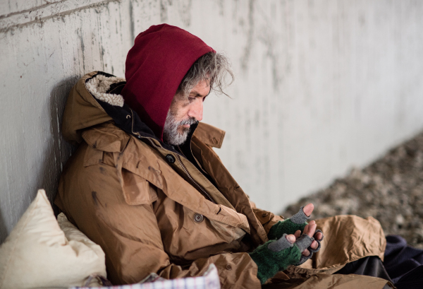 A homeless beggar man sitting outdoors in city asking for money donation.