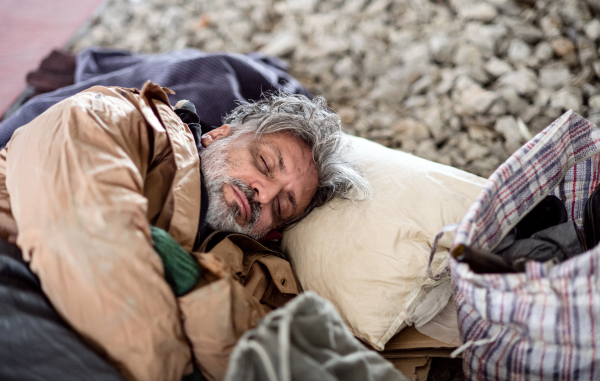 A homeless beggar man lying on the ground outdoors in city asking for money donation, sleeping.