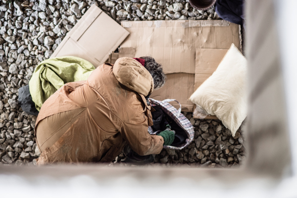 A top view of omeless beggar man standing outdoors with his belongings in city.