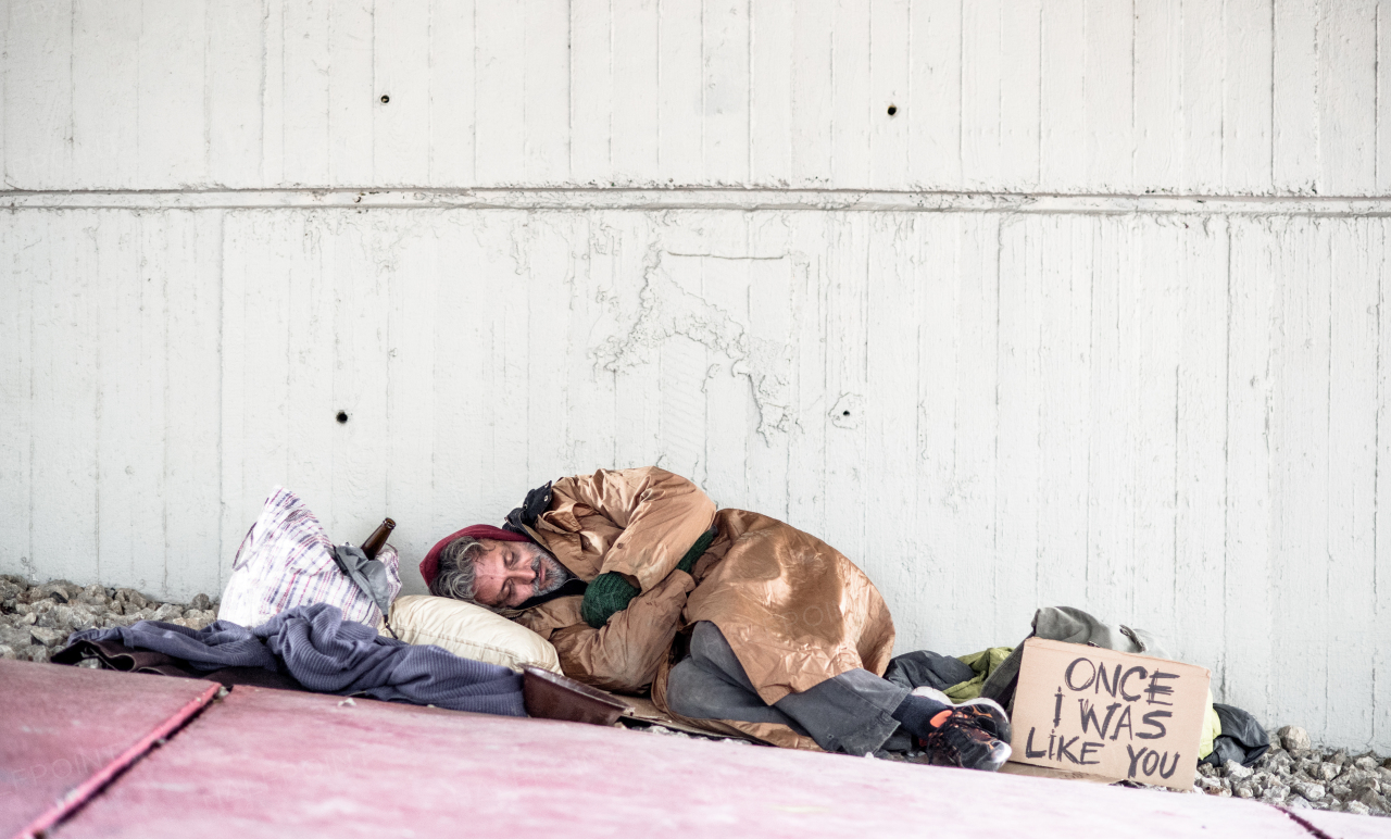 A homeless beggar man lying on the ground outdoors in city, sleeping. Copy space.