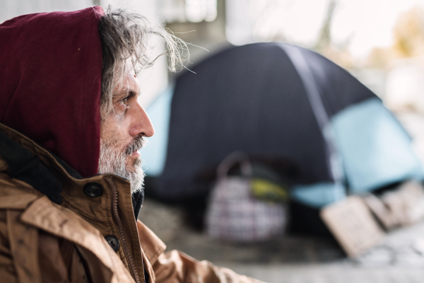 A side view portrait of homeless dirty beggar man sitting outdoors. Copy space.