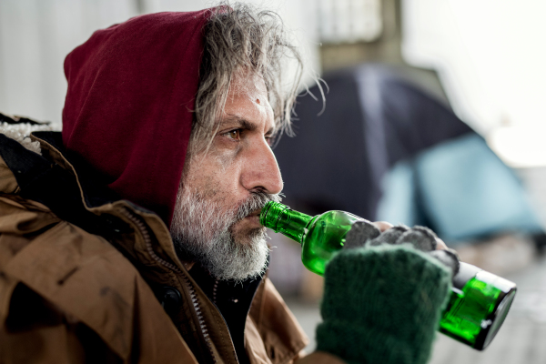 A close-up view of homeless beggar man standing outdoors in city, drinking from a bottle.