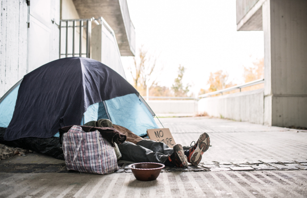 Legs and feet of homeless beggar man lying on the ground outdoors in city, sleeping in tent and asking for money donation.