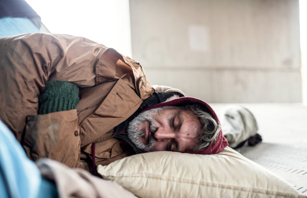 A homeless beggar man lying on the ground outdoors in city asking for money donation, sleeping.