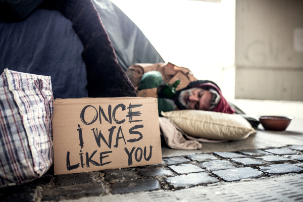 A homeless beggar man lying on the ground outdoors in city asking for money donation, sleeping.