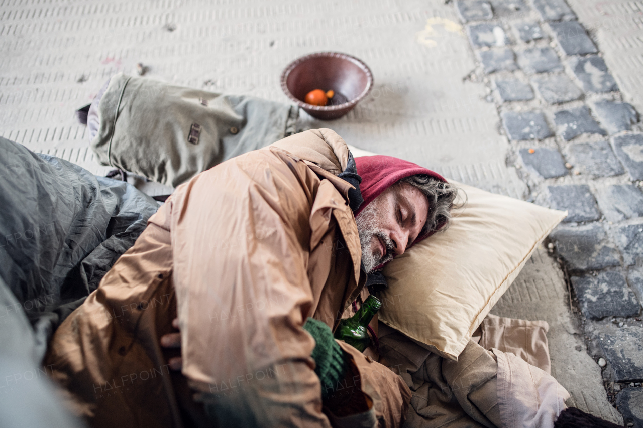 A top view of homeless beggar man lying on the ground outdoors in city asking for money donation, sleeping.