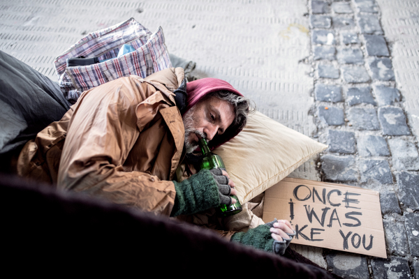 A top view fo homeless beggar man lying on the ground outdoors in city, drinking from the bottle.