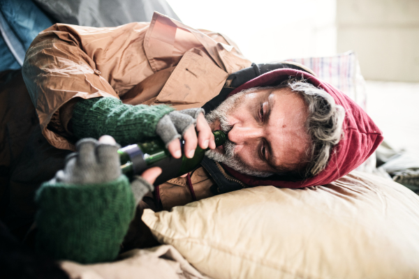 A top view fo homeless beggar man lying on the ground outdoors in city, drinking from the bottle.