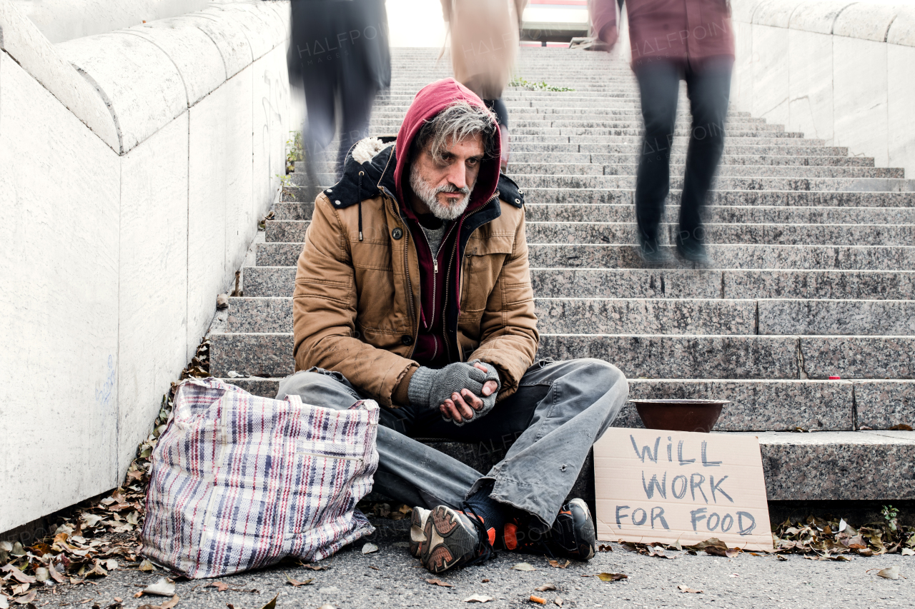 A homeless beggar man with a carboard sign sitting outdoors in city asking for money donation.