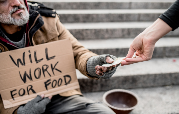 A midsection view of woman giving money to homeless beggar man sitting in city.