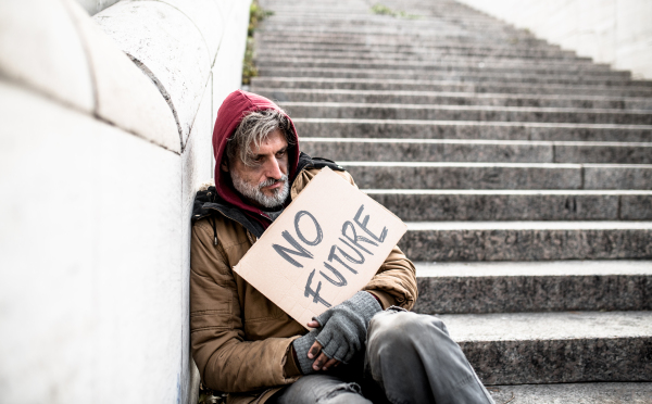 Homeless beggar man sitting on stairs outdoors in city holding no future cardboard sign.