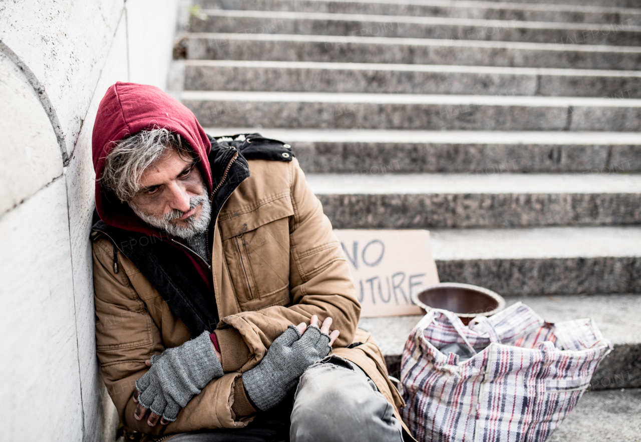 A homeless beggar man sitting outdoors in city asking for money donation.