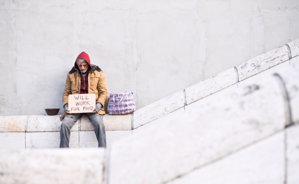 Homeless beggar man sitting outdoors in city holding will work for food cardboard sign, asking for money donation. Copy space.