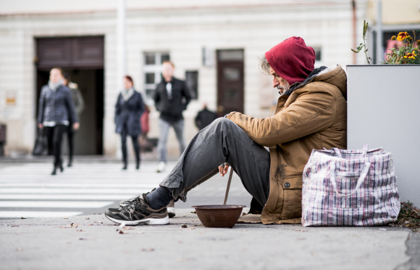 A homeless beggar man sitting outdoors in city asking for money donation. Copy space.