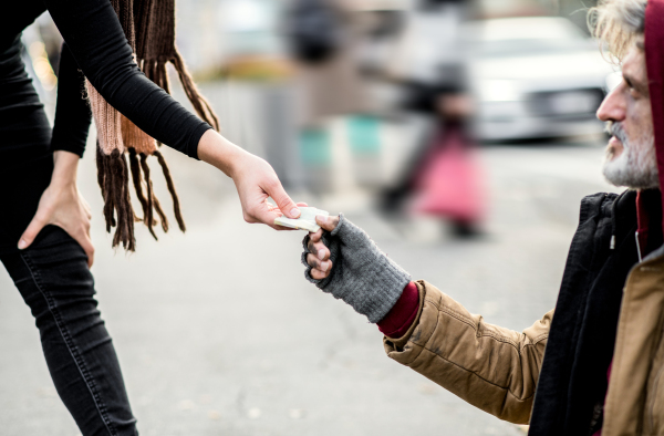 A midsection view of woman giving money to homeless beggar man sitting in city.