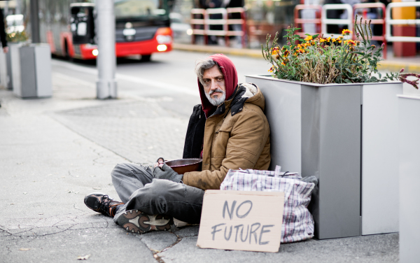 A homeless beggar man with a carboard sign sitting outdoors in city asking for money donation.