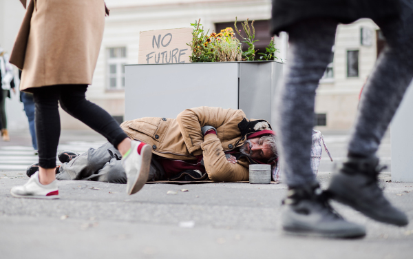 A homeless beggar man lying on the ground outdoors in city, sleeping.