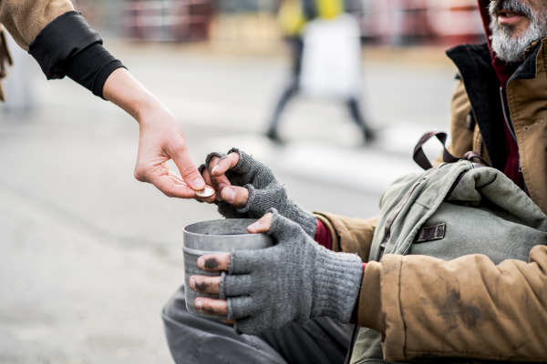 A midsection view of woman giving money to homeless beggar man sitting in city.