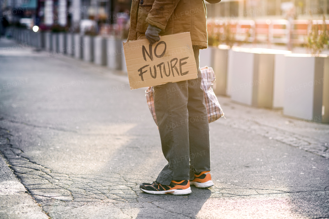 A midsetion of homeless beggar man standing outdoors on a road, holding a bag and cardboard sign. Copy space.