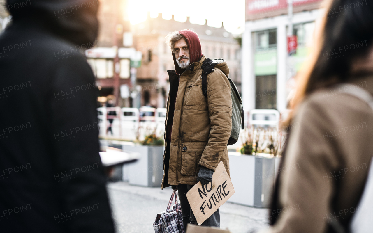 A portrait of homeless beggar man walking outdoors in city, holding bag and no future cardboard sign. Copy space.